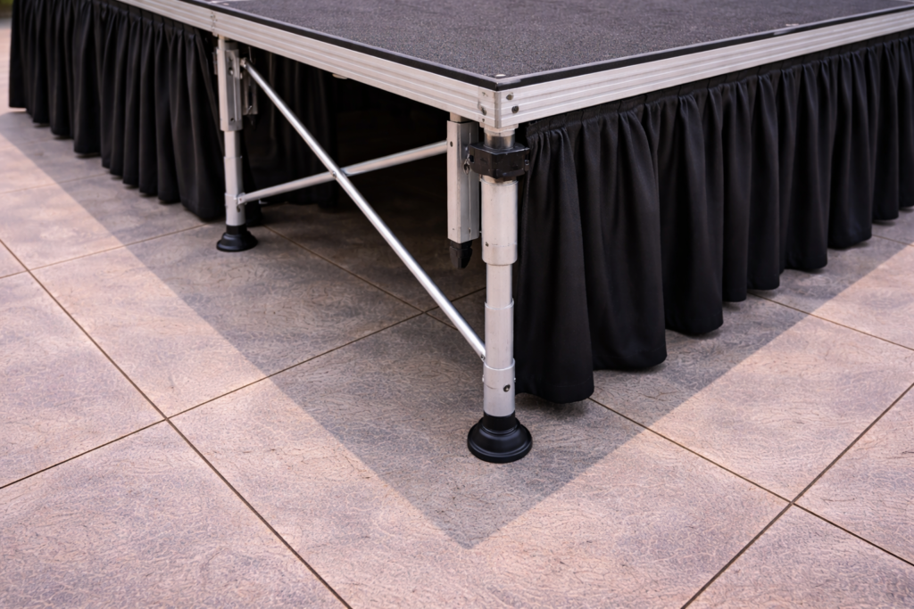 Patas regulables de tarima modular para escenarios, con ajuste de altura y base antideslizante sobre suelo exterior.